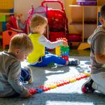 Trzech małych chłopców bawi się na podłodze. Chłopiec klęczy i patrzy sie w obiektyw