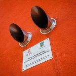 Dwie wystające ze ściany krótkie srebrne rury. Po nimi tabliczka z logotypami i napisem.