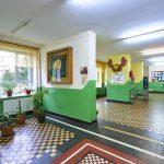 Korytarz w szkole z kolorowymi ścianami i podłogą. Na ścianach obrazy i malunki