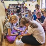 Grupa dzieci siedzi i klęczy na dywanie podczas zabawy