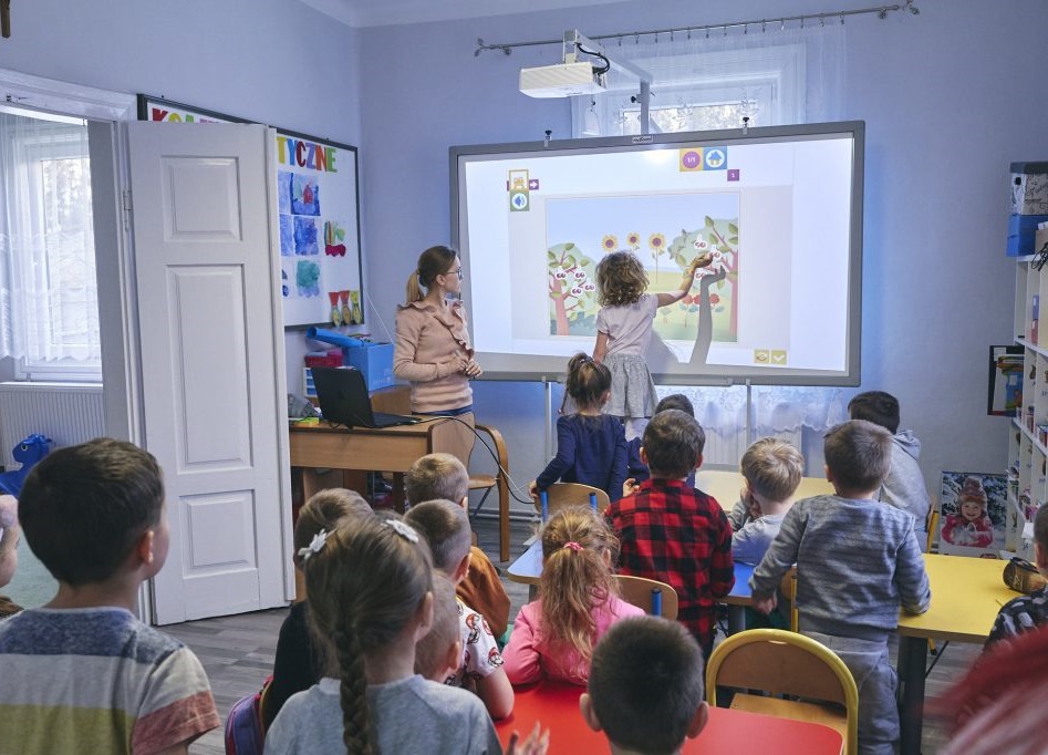 Grupa dzieci w szkole. Jedna dziewczynka korzysta z tablicy interaktywnej.