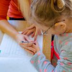Dziewczynka uczy się pisać pod opieką nauczycielki