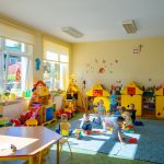 Dzieci bawią się na podłodze kolorowego pomieszczenia. Z tyłu kolorowe szafki