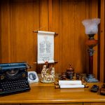 Czarna maszyna do pisania, lampa naftowa i inne eksponaty ustawione na drewnianej półce