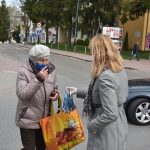 Blond kobieta przekazuje starszej kobiecie maseczkę na ulicy