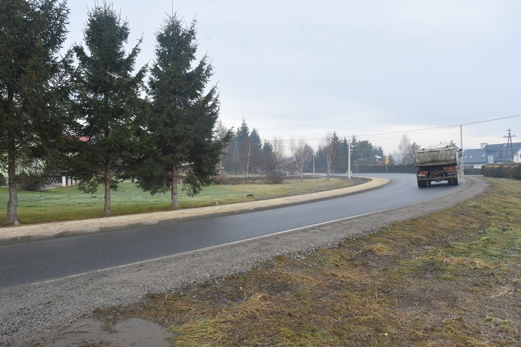 Widok na drogę główną przy której znajduje się nowo wybudowany chodnik oraz po której przejeżdża ciężarówka.
