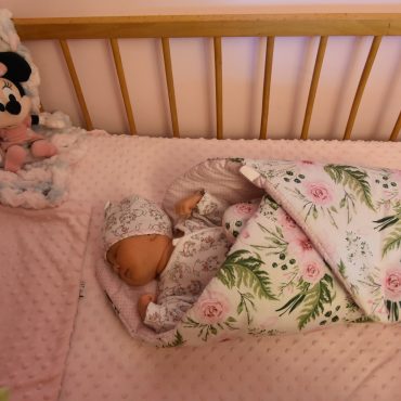 Śpiąca malutka dziewczynka zawinięta w rożek leżąca w łóżeczku drewnianym.