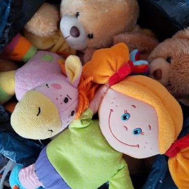 Pluszaki dla dzieci. Wśród nich: szmaciana lalka z pomarańczowymi włosami upiętymi w dwa kucyki. Obok pluszowy osiołek koloru różowego oraz dwa brązowe pluszowe misie.