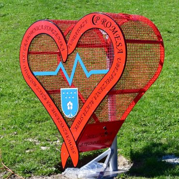 czerwone metalowe serce na nakrętki stoi na trawniku.