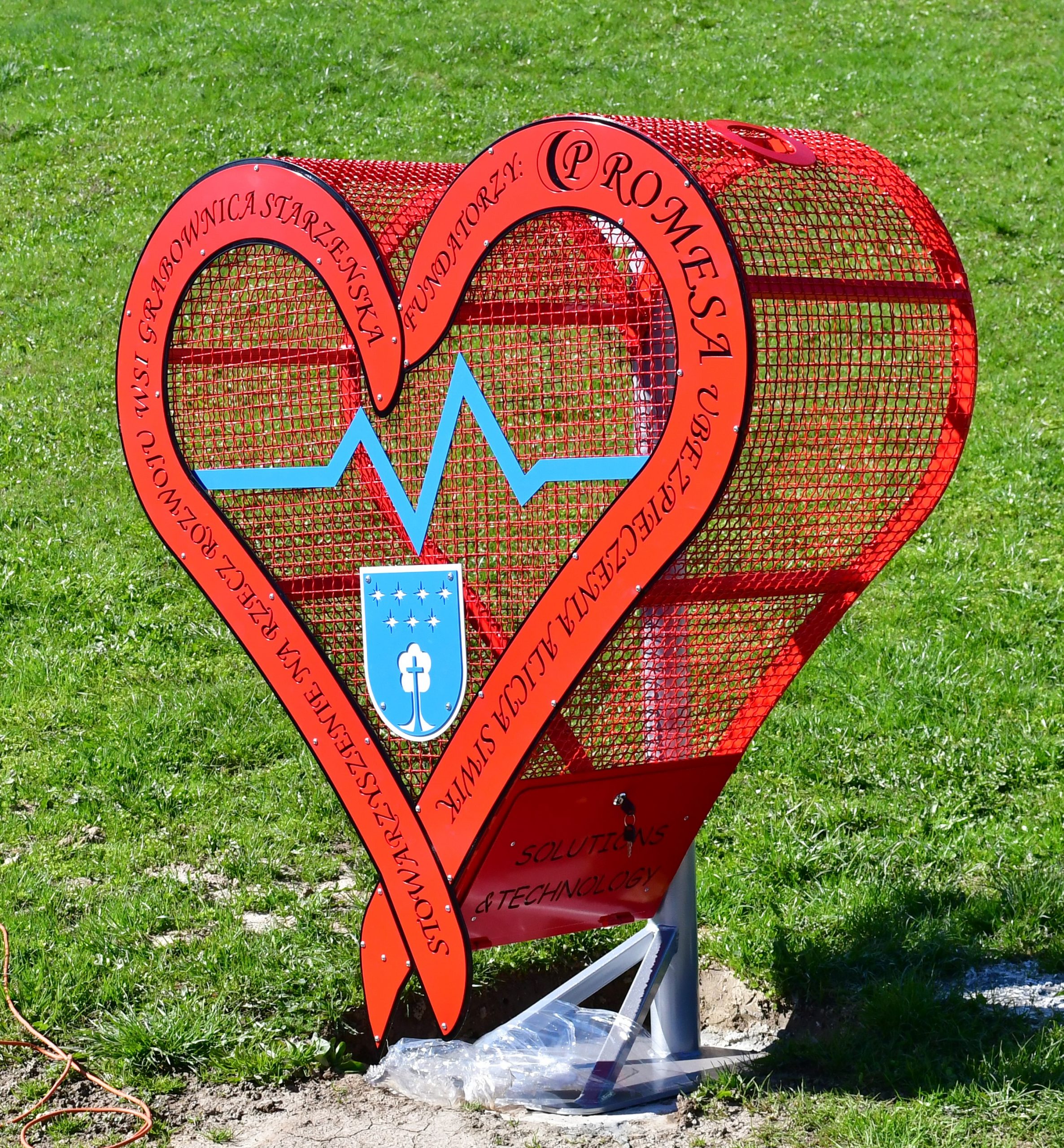 czerwone metalowe serce na nakrętki stoi na trawniku.