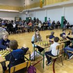 Grupa dzieci przy stolikach na sali gimnastycznej gra w szachy.