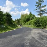 Droga wyłożona nowym asfaltem, po bokach tereny zielone.