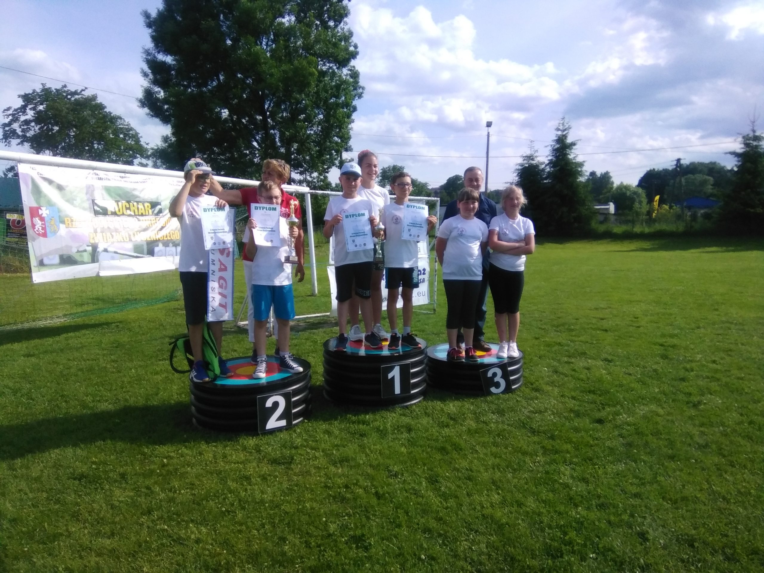 Grupa dzieci ubrana na sportowo stoi na podium z medalami na zewnątrz.