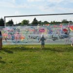 Grupa dzieci maluje farbami na streczu owiniętym na bramce do piłki nożnej na boisku.