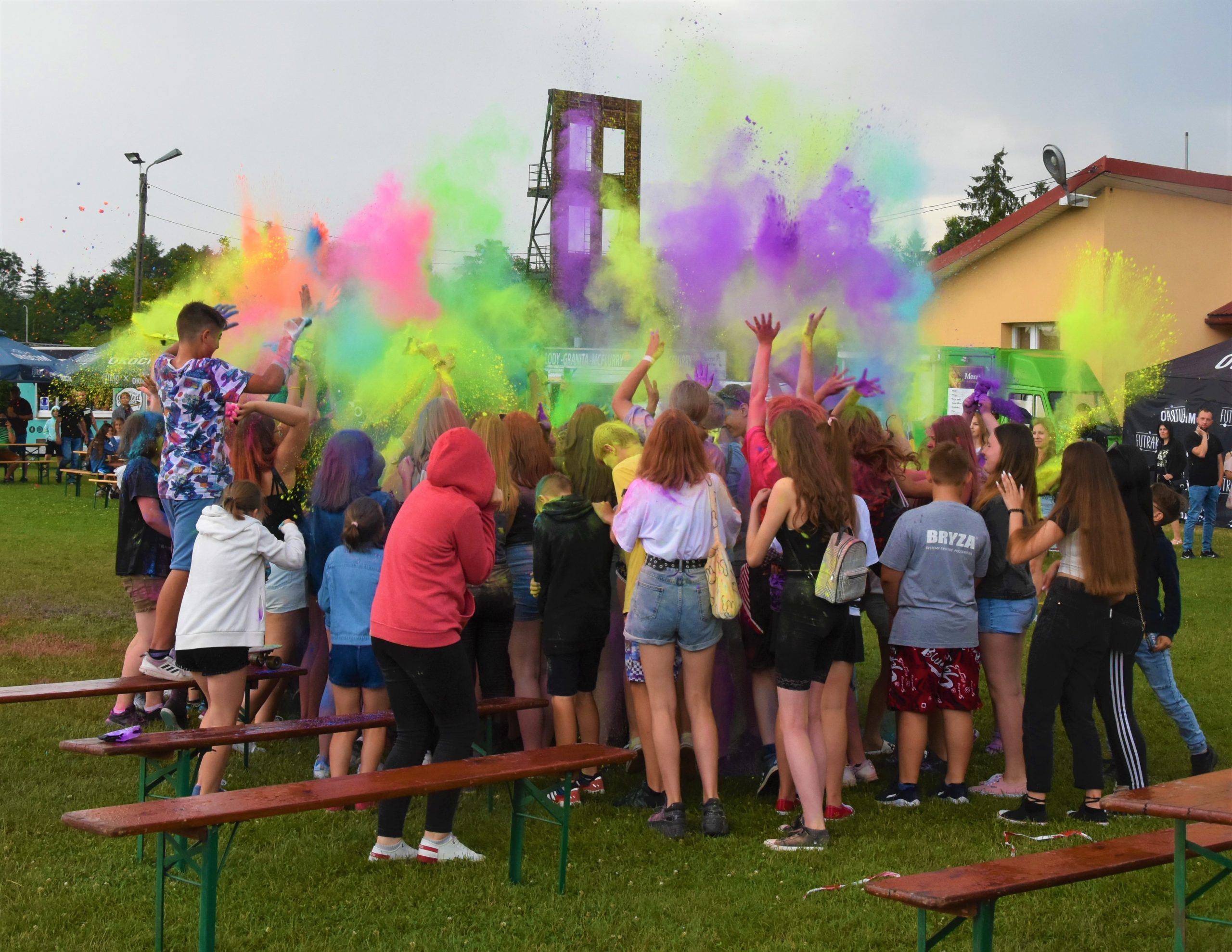 Ciasno stłoczona grupa młodych osób, wyrzucająca w powietrze kolorowe proszki.