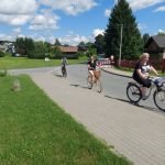 Trzy osoby jada na rowerze po drodze asfaltowej.