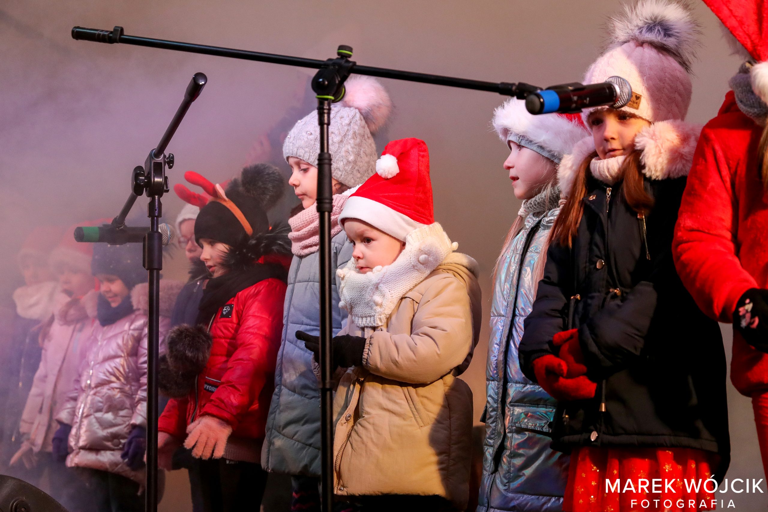 Dzieci ubrane w czerwone czapki śpiewają podczas spotkania z Mikołajem