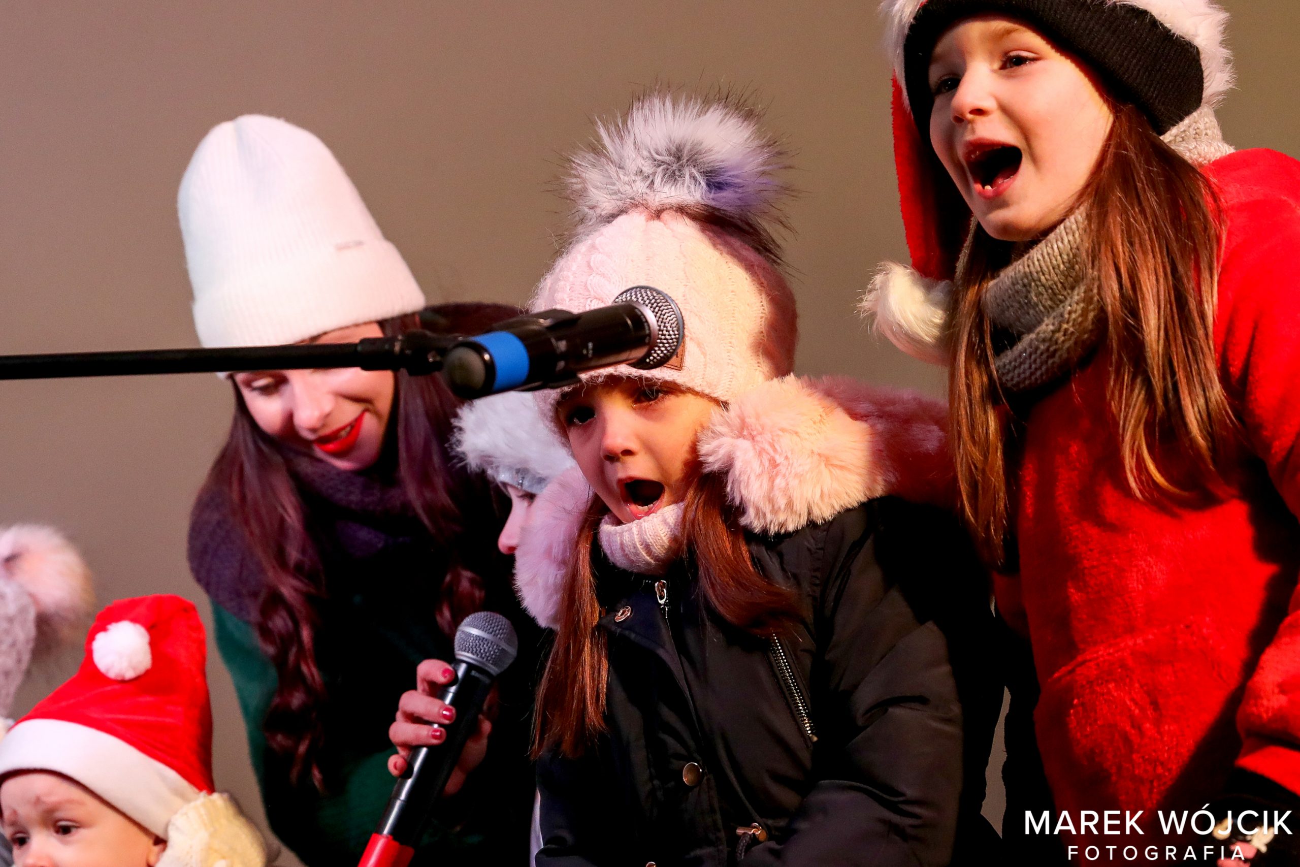 Dzieci ubrane w czerwone czapki śpiewają podczas spotkania z Mikołajem