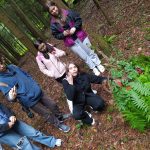Grupa młodzieży w lesie. Jedna z dziewcząt wskazuje na paproć.