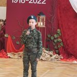 Młody chłopak przebrany w strój żołnierza recytuje wiersz na sali gimnastycznej.