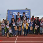 Duża grupa dzieci i młodzieży stojąca na stadionie z dyplomami. Z tyłu widać baner promocyjny UKS.