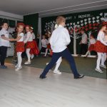 Grupa dzieci ubranych w odświętne stroje tańczy w sali pzredszkolnej.