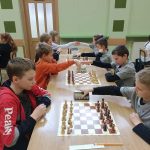 Grupa dzieci różnej płci i wieku grajaca w szachy na rozleglej sali.