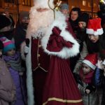 Osoba ubrana w stój św. Mikołaja z worem prezentów na rynku. Wokół wdać dorosłych i dzieci.
