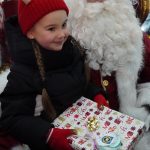 Młoda dziewczynka w zimowym stroju otrzymuje prezenty od św. Mikołaja.
