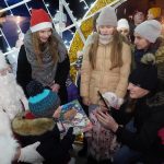 Grupa dzieci w zimowych strojach otrzymuje prezenty od św. Mikołaja.