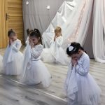 Dziewczynki przebrane w białe spódniczki i koszulki tańczą na sali przedszkolnej