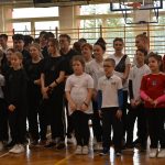 Grupa dzieci i młodzieży stojaca na sali gimnastycznej