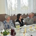 Grupa starszych osób zasiadajaca za zastawionym stole na sali.