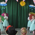 Grupa czterech dziewczynek z parasolkami na scenie w czasie wystepu artystycznego.