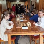 Grupa dzieci grająca w szachy w pomieszczeniu.