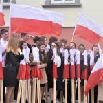 Duża grupa dorosłych i młodzieży z polskimi flagami stojący na rynku.