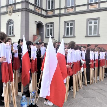 Duża grupa młodzieży z polskimi flagami stojąca na rynku.