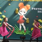 Grupa dwóch dziewczynek w rózowych sukienkach wykonująca układ taneczny.