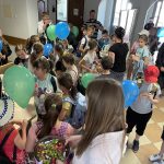 Grupa dzieci z balonami i dorośli stoją w korytarzu