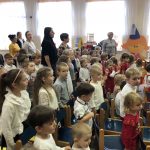 Grupa dzieci stoi na baczność w sali przedszkolnej i spiewają hymn państwowoy.