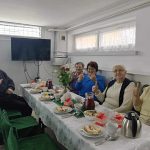 Grupa starszych kobiet siedzi przy stole swiatecznym i smieją się do siebie.