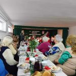 Grupa starszych kobiet siedzi przy stole swiatecznym i smieją się do siebie oraz ogladają występ dzieci.