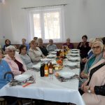 Grupa starszych kobiet ubranch w odświetne stroje siedzi przy swiatecznym stole.