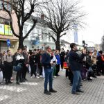 Grupa młodzieży stoi na placu przed urzędem w centrum miasta.