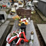 Grób na cmentarzu, na nim stoją znicze i wiązanka kwiatów biało-czerwona.