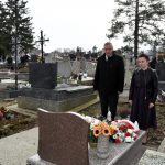 Starszy mężczyzna w garniturze i młoda kobieta stoją przy grobie na cmentarzu.